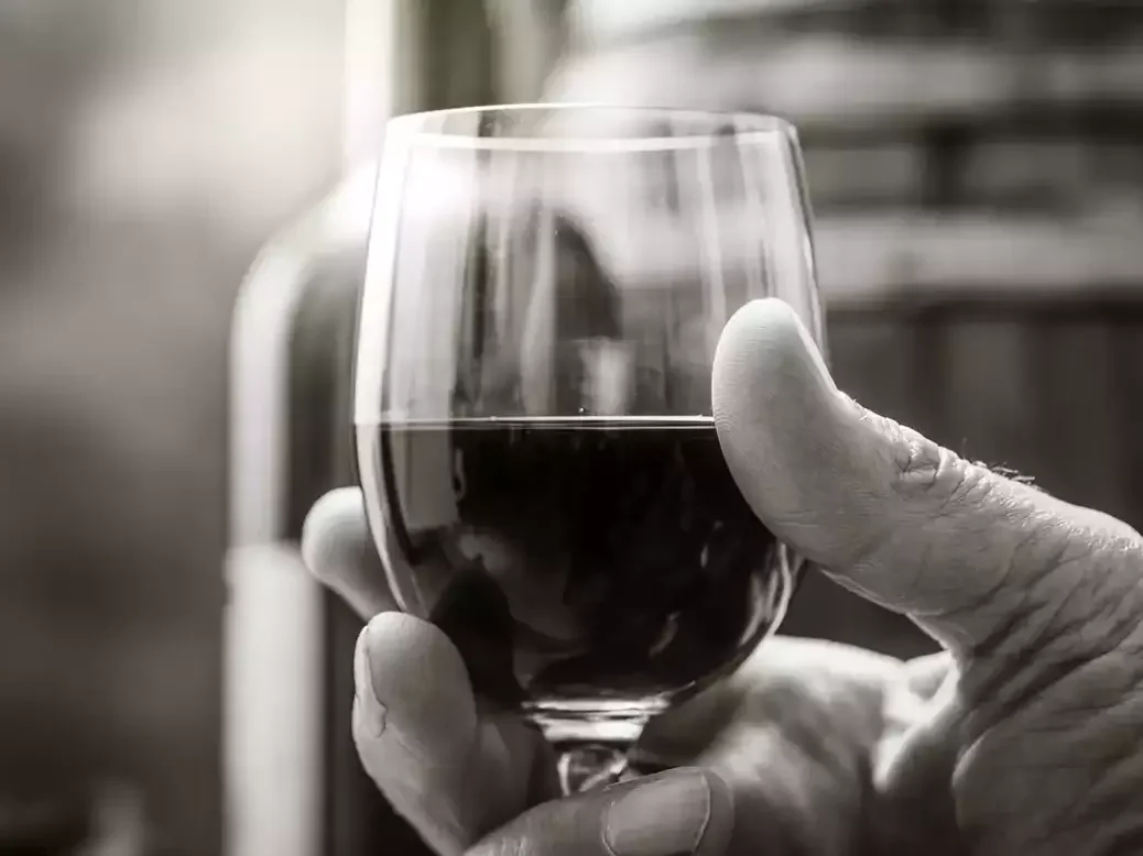 A glass of wine in a senior man's hand illustrating long life expectancy