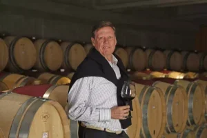 Aurelio Montes with a glass of wine and some barrels