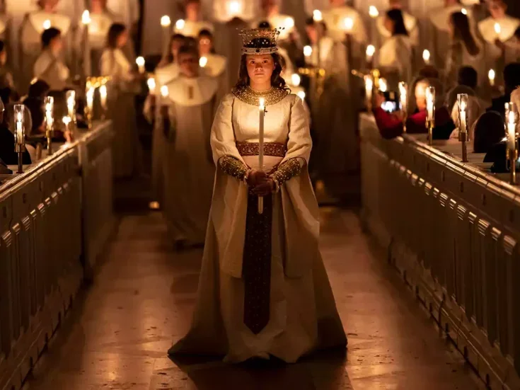 A woman holding a candle in a church with lots of candles on Santa Lucia Day