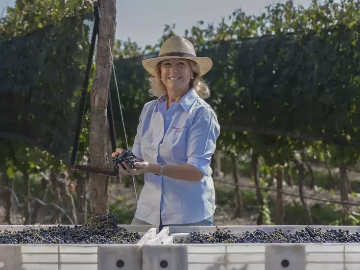 Susana Balbo holding a bunch of grapes in a vineyard