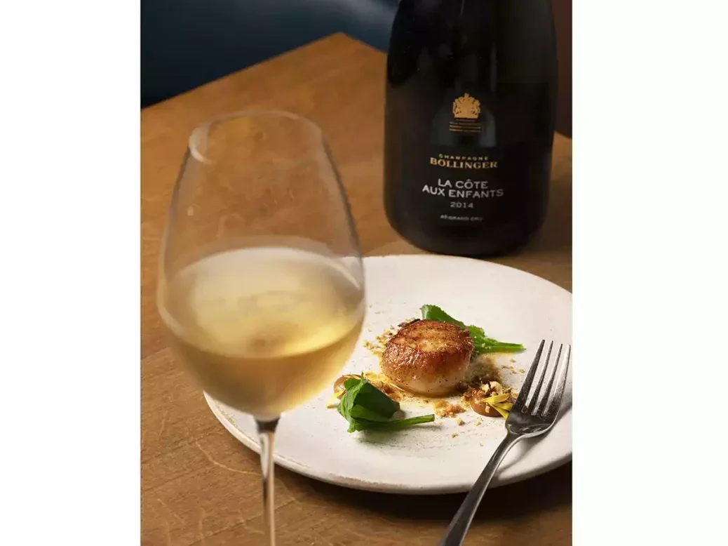 A bottle of Bollinger with a glass of Champagne and a plate with scallops