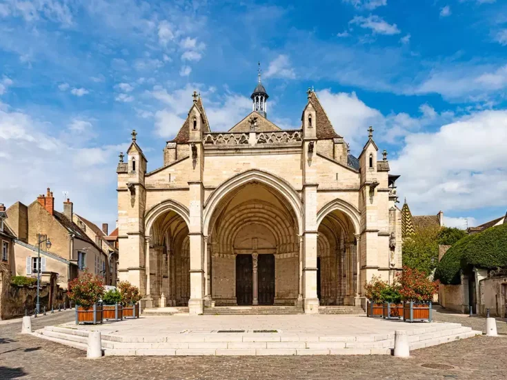 The front of the Basilica Nortre Dame in Beaune, with small place in front of it and low-rise stone buildings either side.