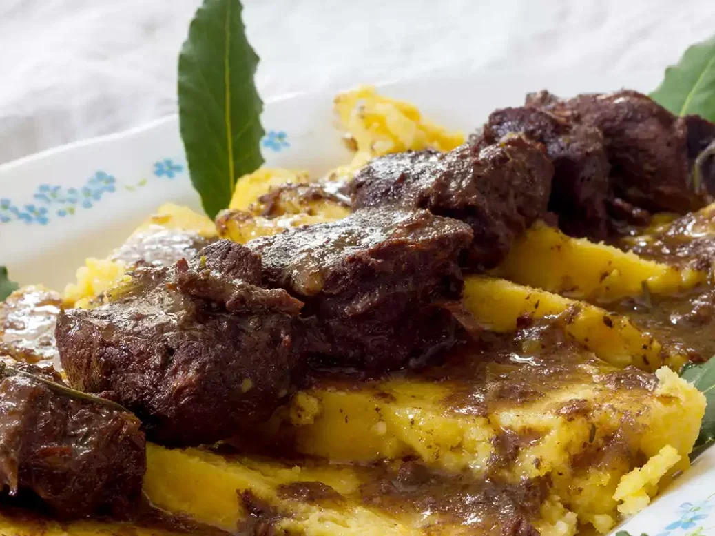 Civet de sanglier boar stew served on top of polenta pieces with bay leaves on a plate.