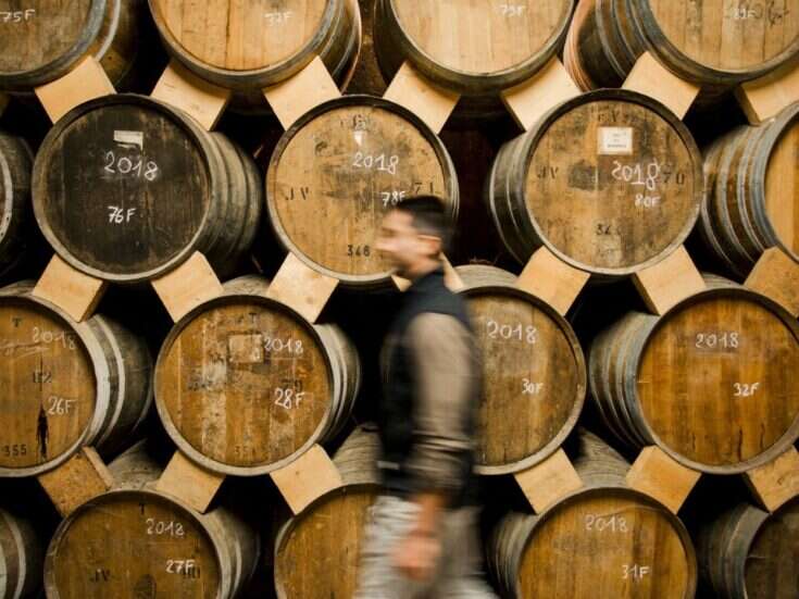 A man walks in front of stacked barrels of Cognac