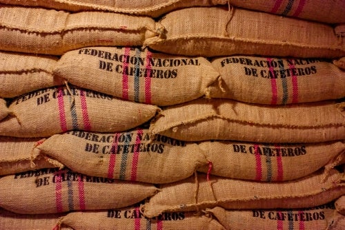 Stacks of hessian sacks of coffee beans branded with the words "Federacion Nacional de Cafeteros" and green and red stripes.