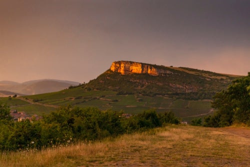 white limestone cliff outcrop of Vergisson reflecting orange in the sunshine above vineyards and a hazy sunset sky.