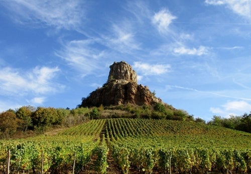 A rocky outcrop against a blue sky with little fluffy white sky above vineyards in Pouilly-Fuissé in the Mâconnais