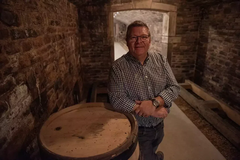 Bernard de Villaine leaning on a barrel in a cellar