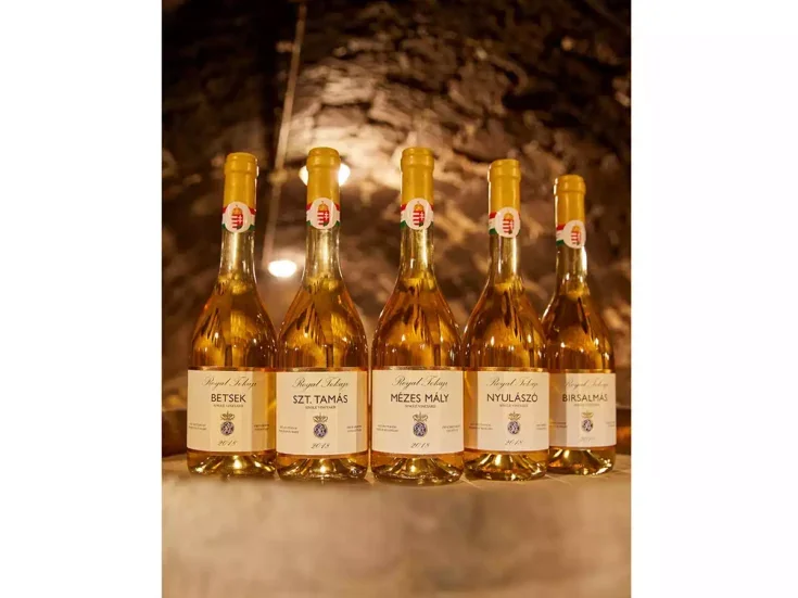 Five bottles of golden Royal Tokaji wine on a stone table in a brick cellar