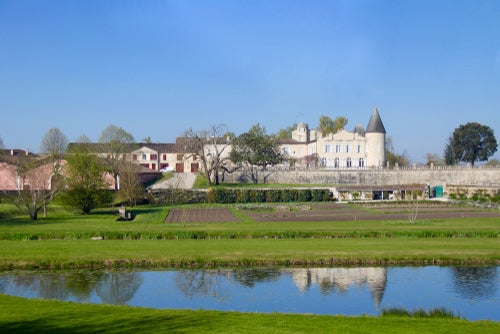 A view of Château Lafite-Rothschild on a sunny day with blue skies, with the building reflected in a pond in the foreground