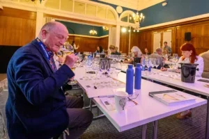 Tasters at the Battle of the Bubbles sitting at a white table sniffing glasses of Champagne and taking notes