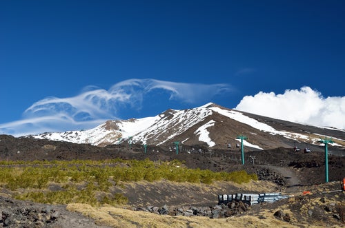 A vineyard with very old bush vines on the lower slopes of Mt Etna with snow-capped peaks and a blue sky in the background