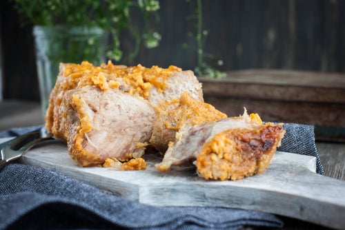 pork braised in milk in one piece on a marble slab with a knife and a glass of herbs in the background