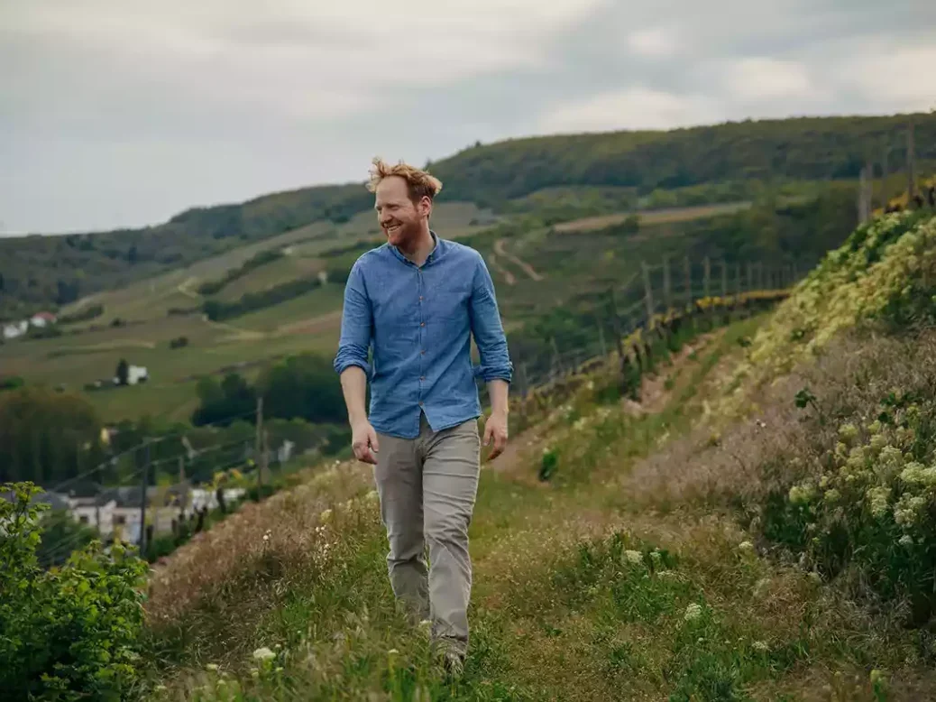Georg Rumpf, with red hair in a blue shirt and khaki chinos, walking in his vineyards