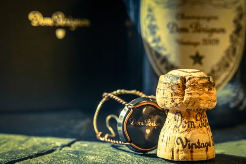 A Champagne cork and its cage in front of a bottle and box of Dom Pérignon