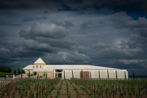 A view of Château Bélair-Monange, a limestone building with a short white turret, vines in the foreground