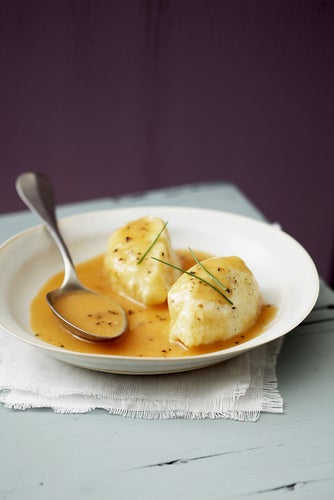 two quenelles with sauce and a spoon in a bowl on a white cloth on a grey table with a black background
