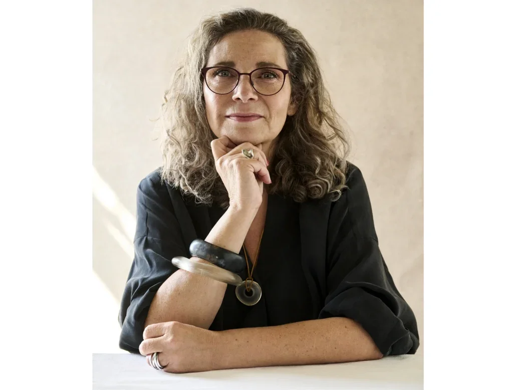 Natasha Hughes in glasses and a dark top sitting at a table with one hand under her chin