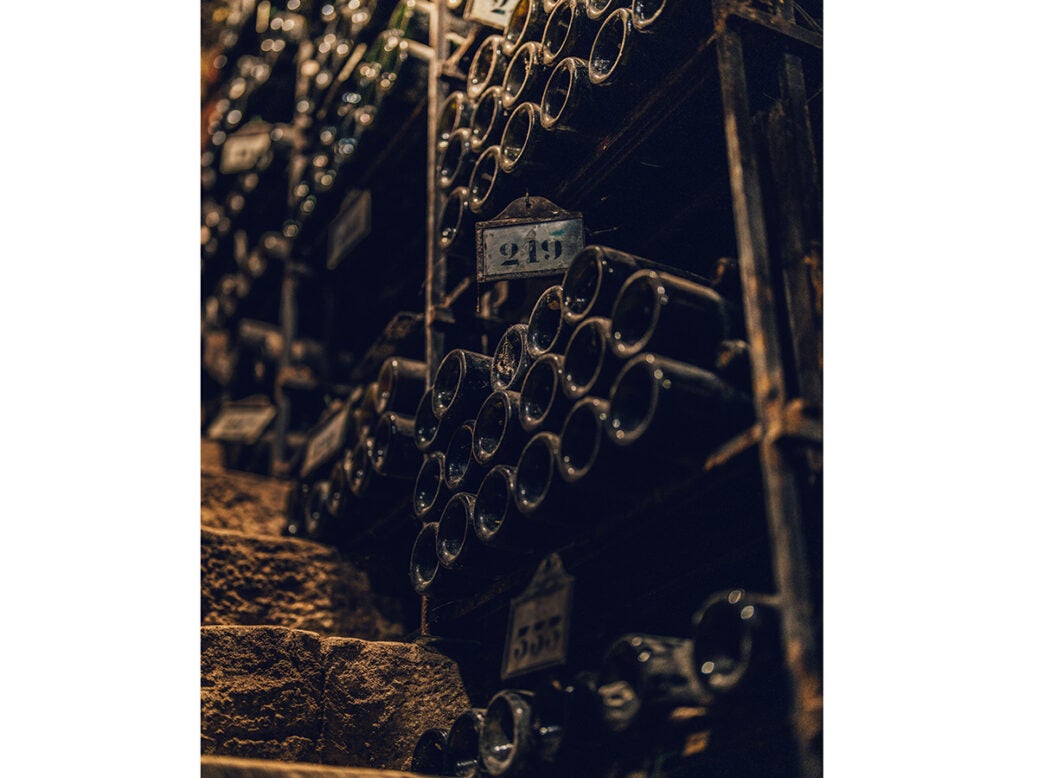 Dusty bottles in stacks by a staircase in a dark cellar