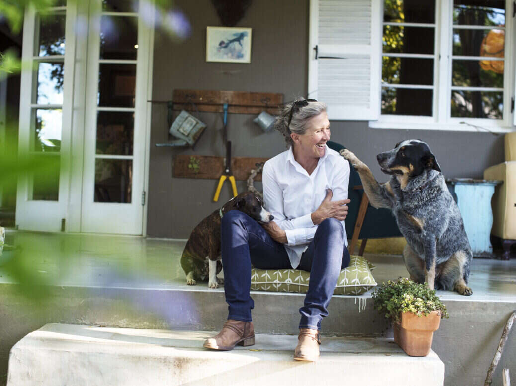 Rosa Kruger in white shirt and jeans sitting on her porch with two dogs