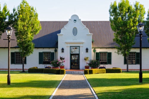 A colonial-style low white building, smartly painted, with a path in front, and a curvy Dutch style front entrance.