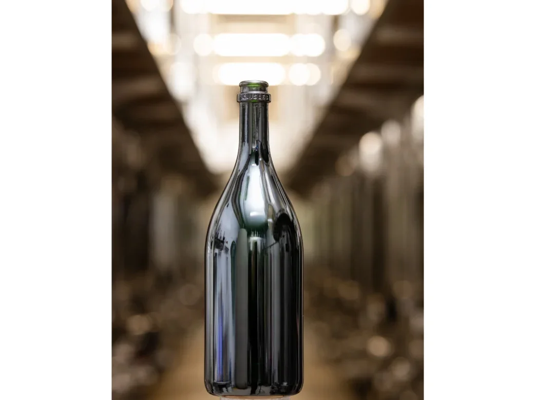 An empty Light-26 sparkling wine bottle that seems to float in the air in a winery on a clear perspex plinth
