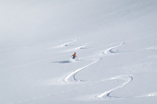 aerial view of a woman skiing in an s-shape through white snow in the sunshine