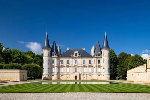 Grand château in Pauillac with slate tiled roof with turrets and limestone building with a smart front lawn on a sunny day