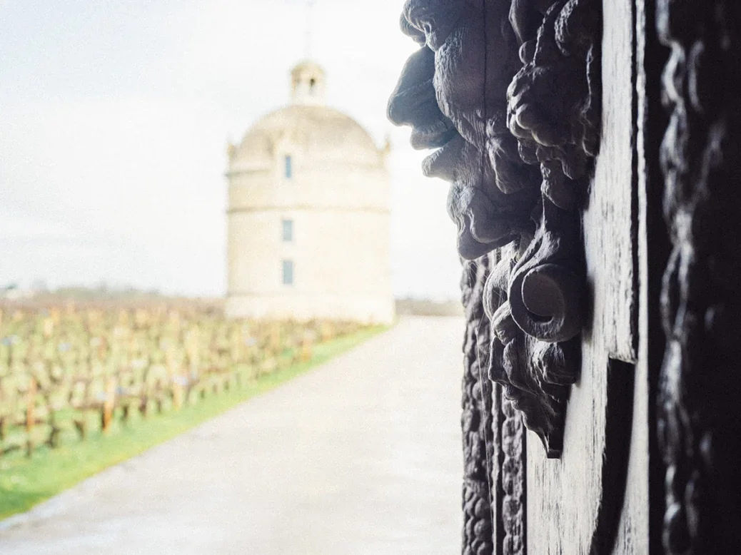 The gate at Latour, with a metal sculpted face in relief, and then a view of Latour at the end of a path with the vines to the left