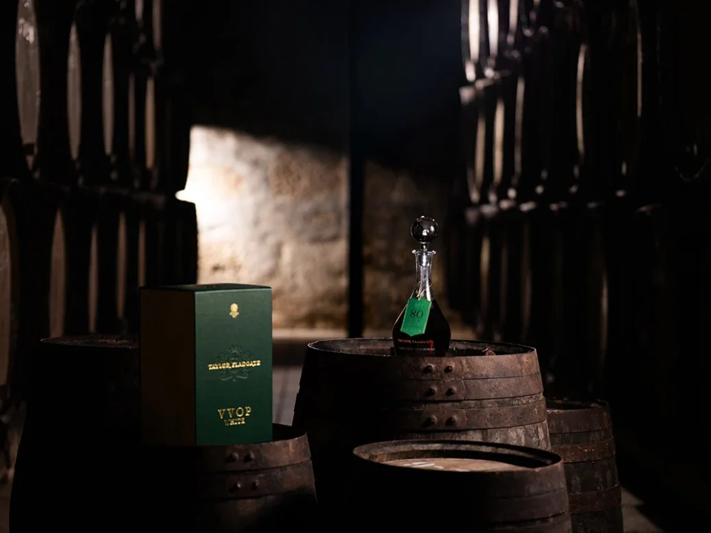 a decanter-like bottle of Taylor's Very Very Old White Port sitting on a barrel in a dark cellar illuminated by a shaft of daylight
