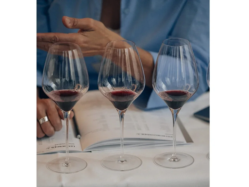 Three glasses of PInot Noir / Spätburgunder in front of a notebook and a man in a blue shirt with a tie, just the close up of his hands behind the glasses